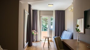Une chambre d’hôtel moderne avec un plancher en bois, une table à manger, un canapé et une grande fenêtre avec des rideaux.
