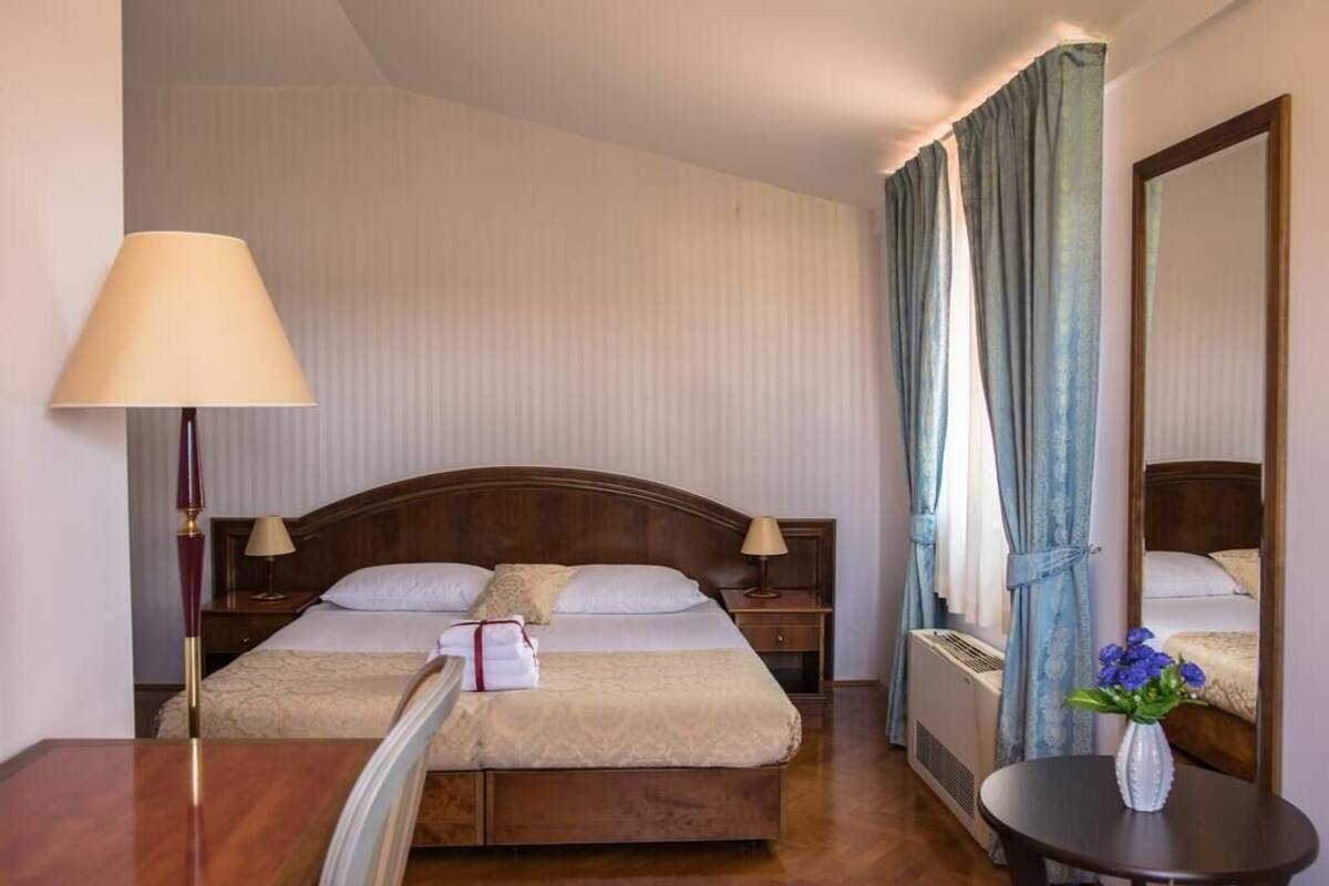 Une chambre d’hôtel avec deux lits, une tête de lit en bois, des lampes de chevet, une table avec un vase et un miroir.