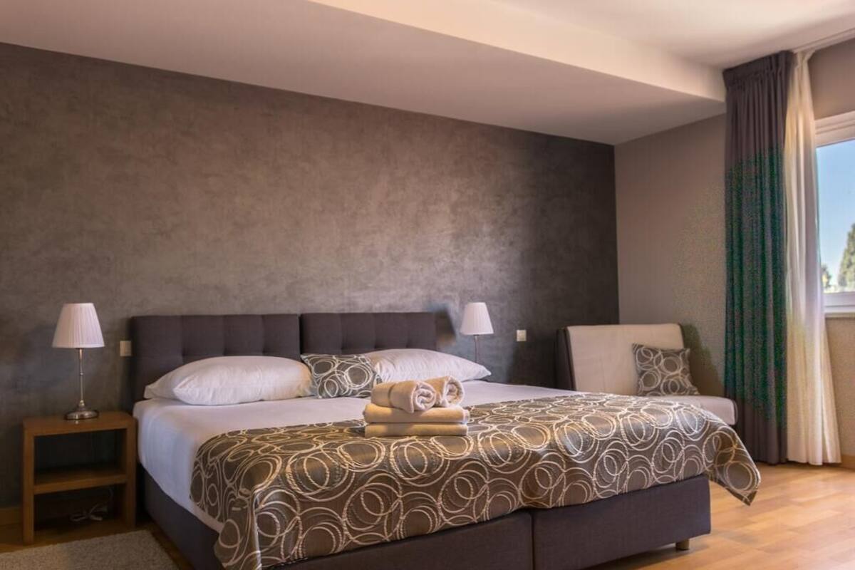 Une chambre d’hôtel moderne avec un grand lit, deux tables de chevet et une vue sur l’extérieur.