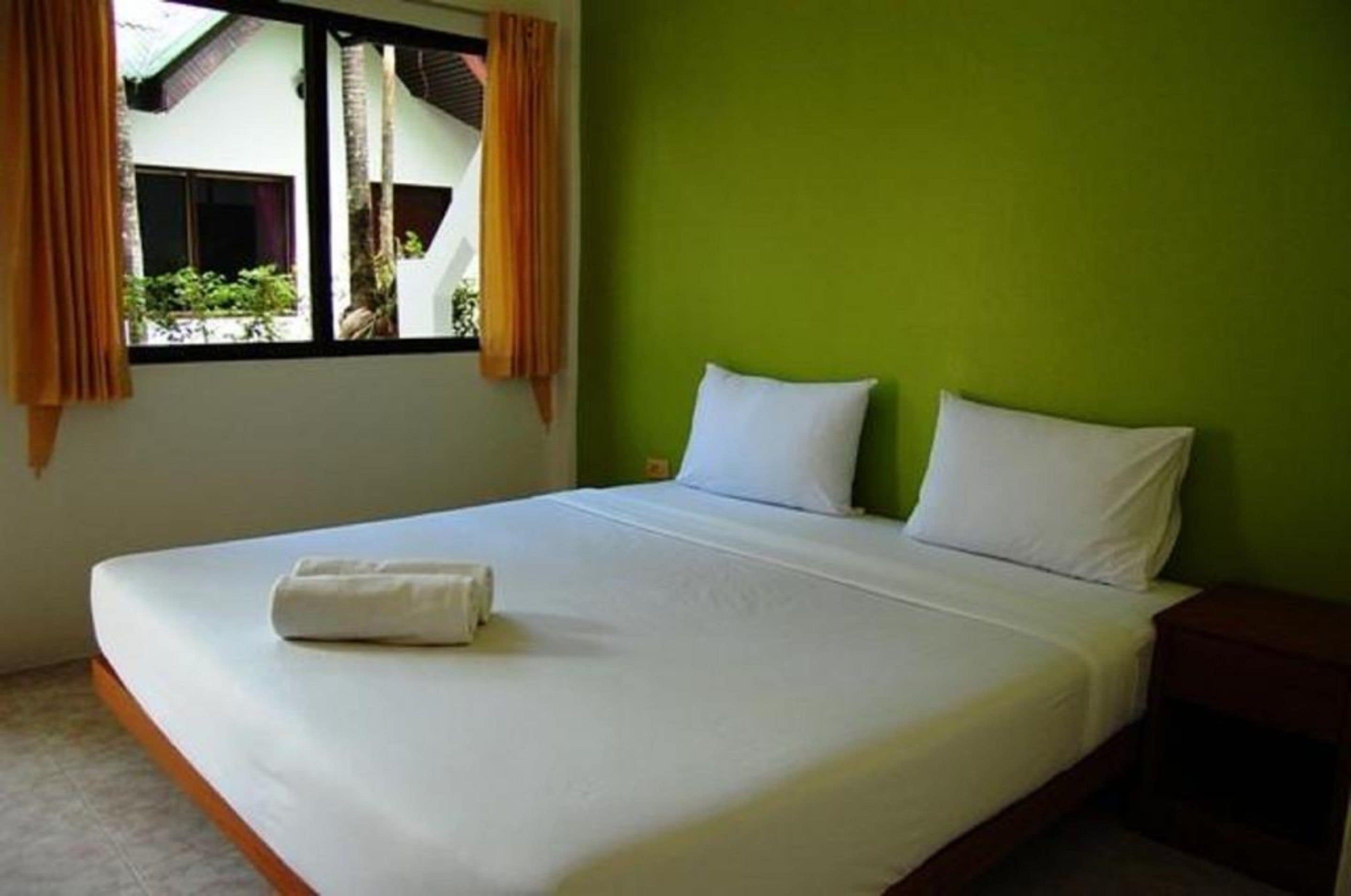 A single-bed room with a green wall, white bedding, and a window with curtains.