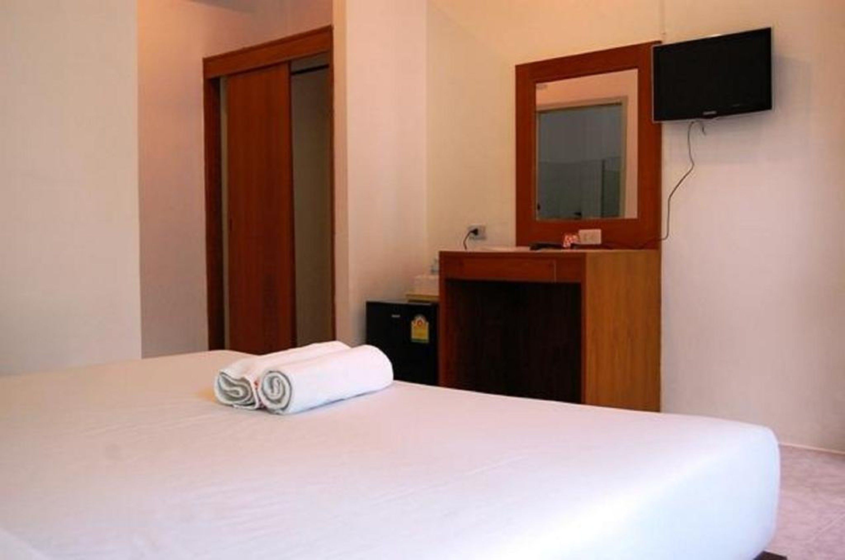A hotel room with a bed, a wooden dresser, a mirror, and a flat-screen TV mounted on the wall.