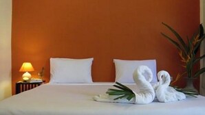 Une chambre d’hôtel avec un lit, des oreillers blancs, une table de chevet avec une lampe et une serviette décorative pliée en forme de cygne.