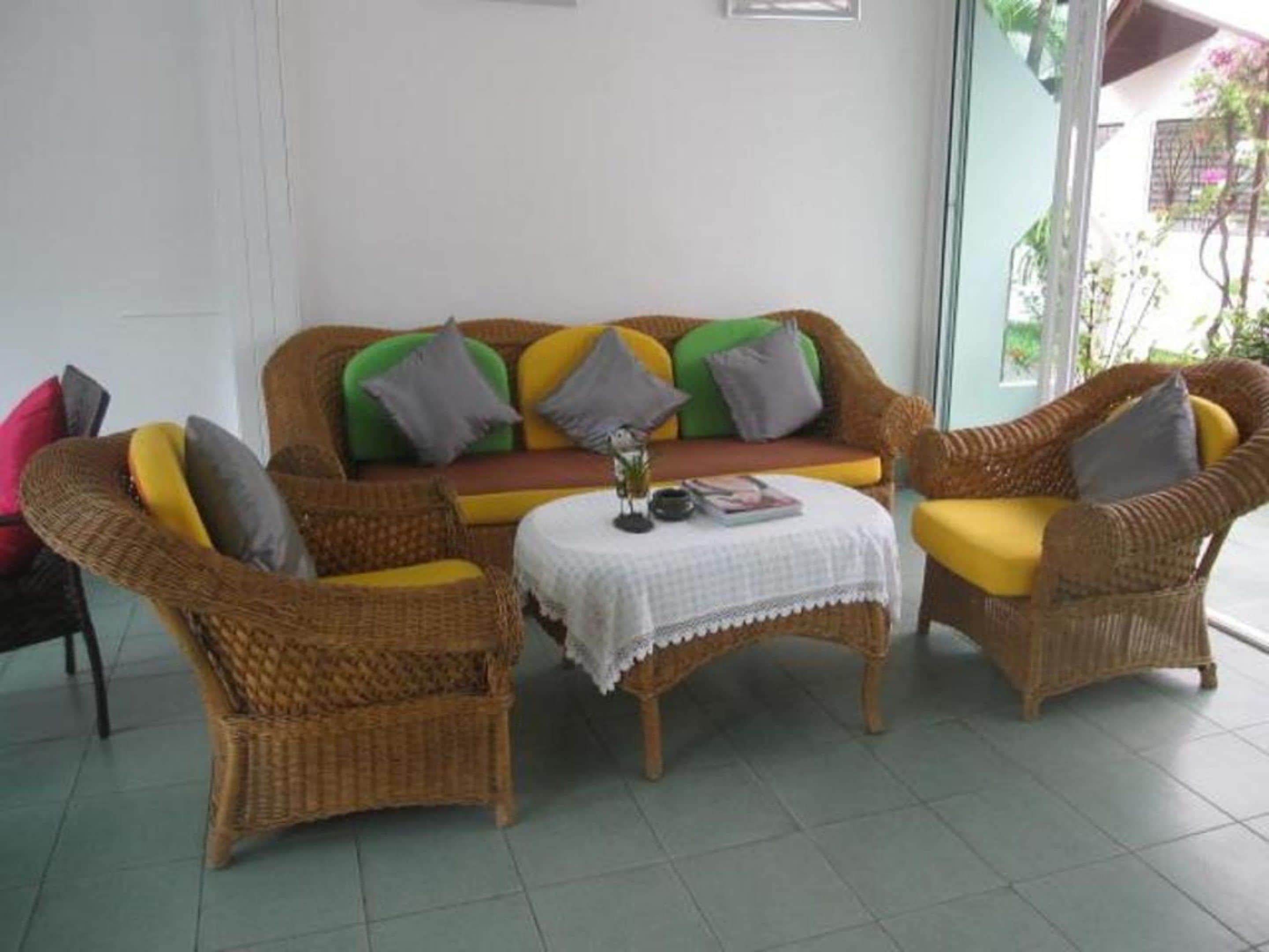 A wicker sofa with cushions in various colors, a small table with a white tablecloth, and chairs with yellow cushions.