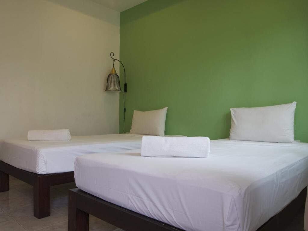 Two single beds with white linens and pillows, a green accent wall, and a hanging lamp.