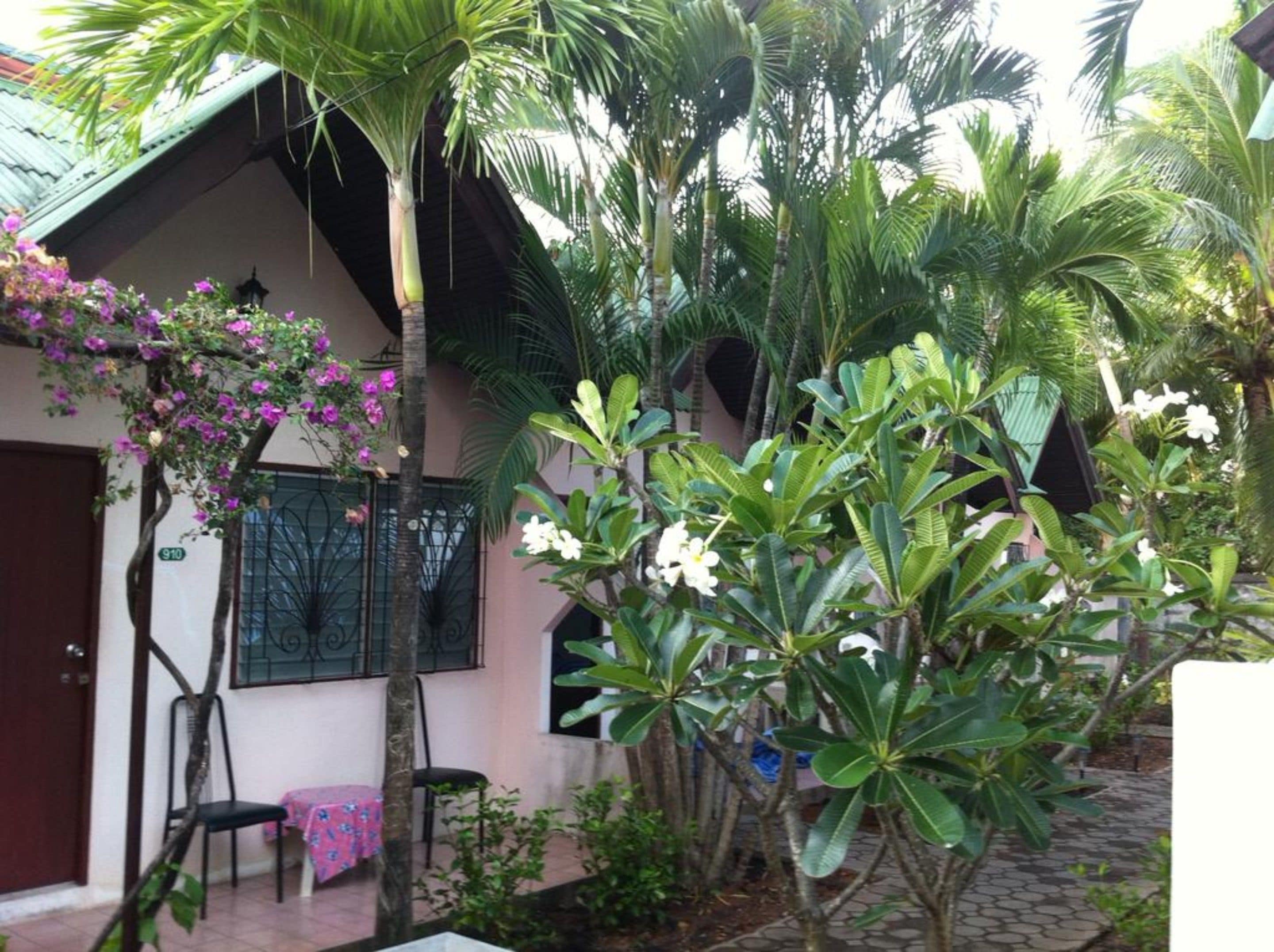 A house with a tiled roof, a door, and a window with a metal grill. There are plants and flowers around the house.