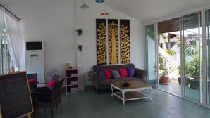 Un salon comprenant un canapé, une table basse et une grande fenêtre. On y trouve également un ventilateur de plafond, un climatiseur mural et un panneau décoratif sur le mur.