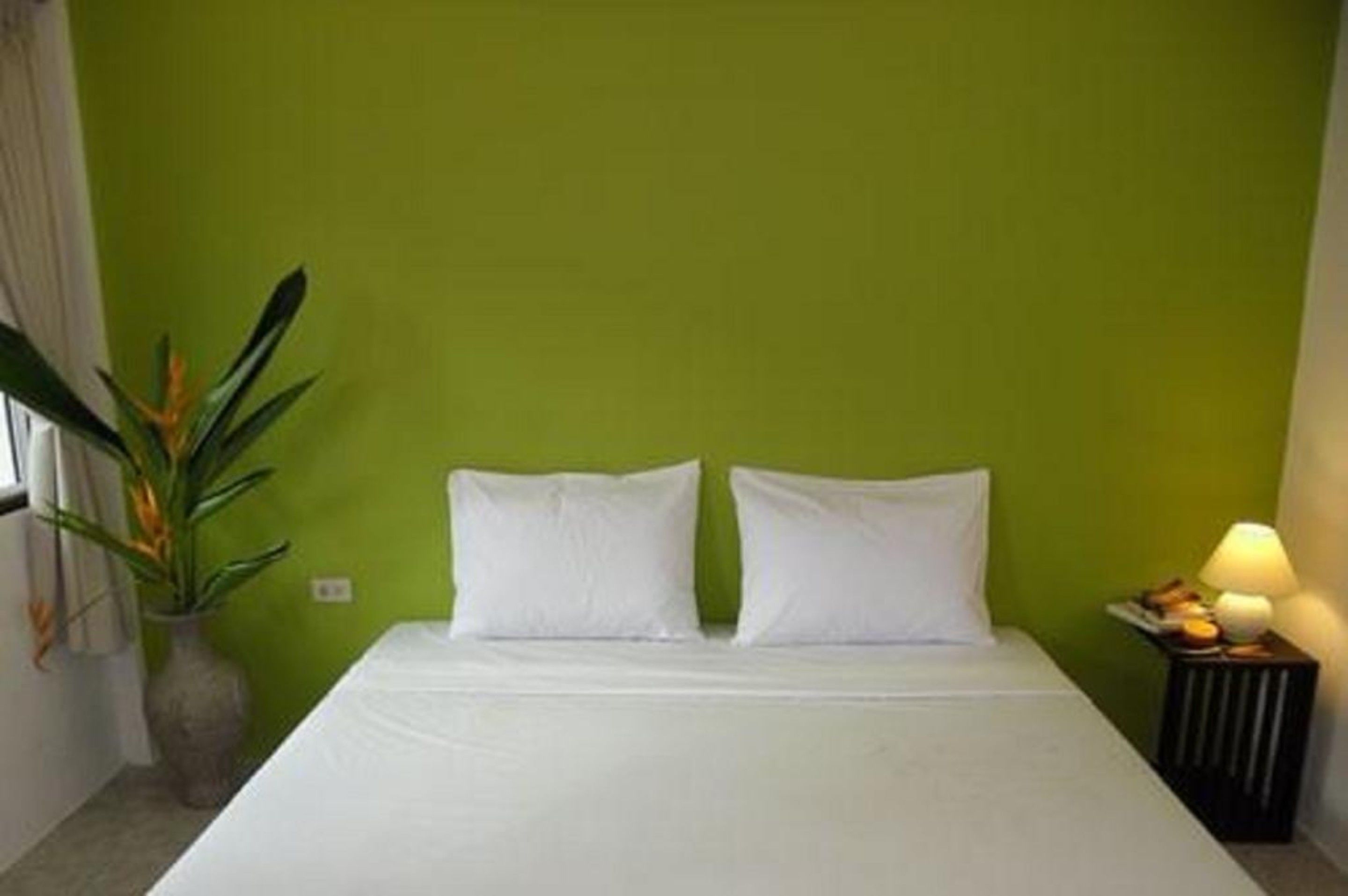 A bed with white linens, a green wall, and a nightstand with a lamp and a plate of food.