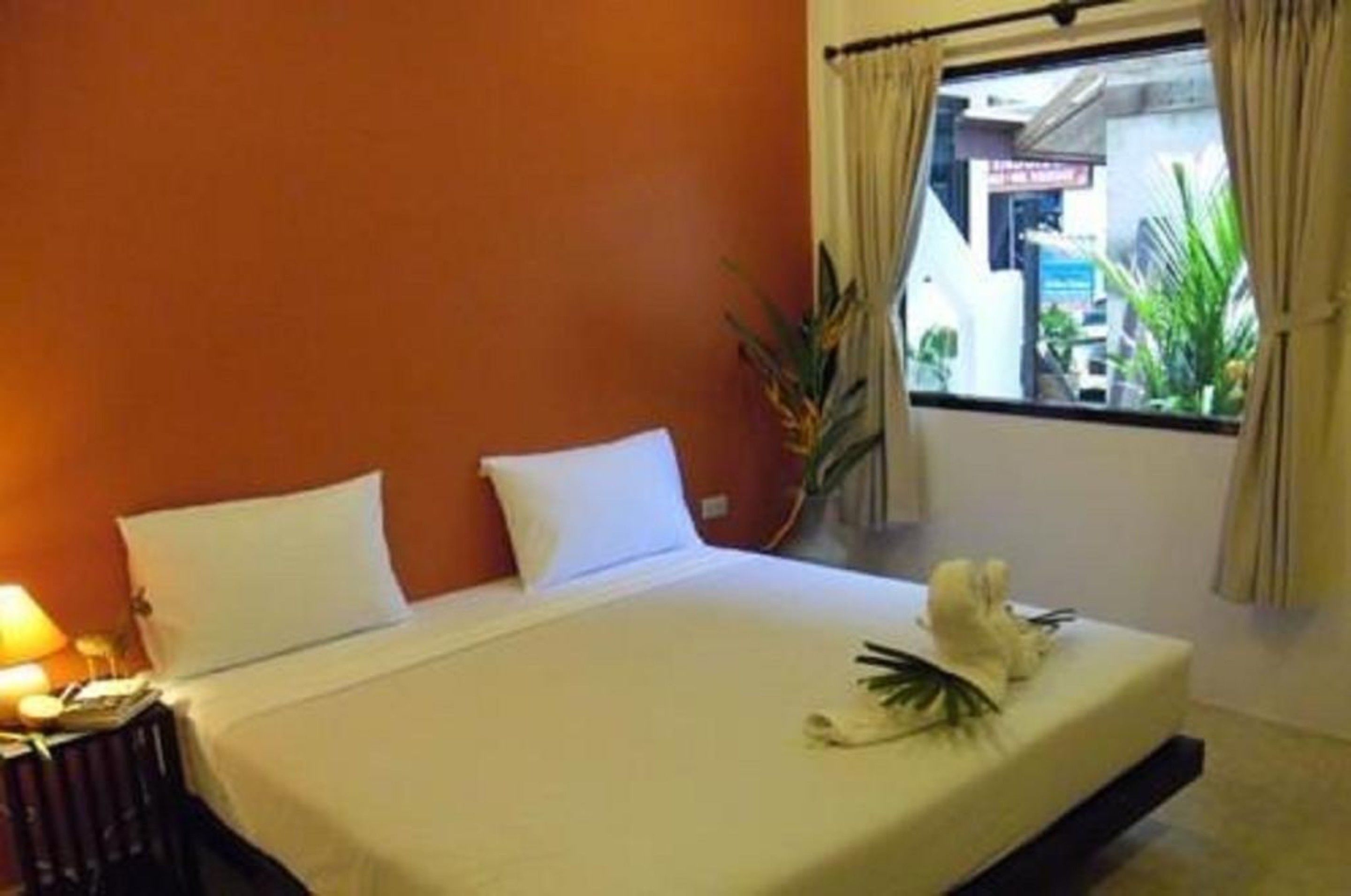 Une chambre d’hôtel avec un lit, des oreillers blancs, une lampe de chevet et une fenêtre avec des rideaux.