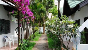 Un sentier bordé d’une végétation luxuriante et de plantes en fleurs, qui mène à un bâtiment blanc doté d’un toit en tuiles.