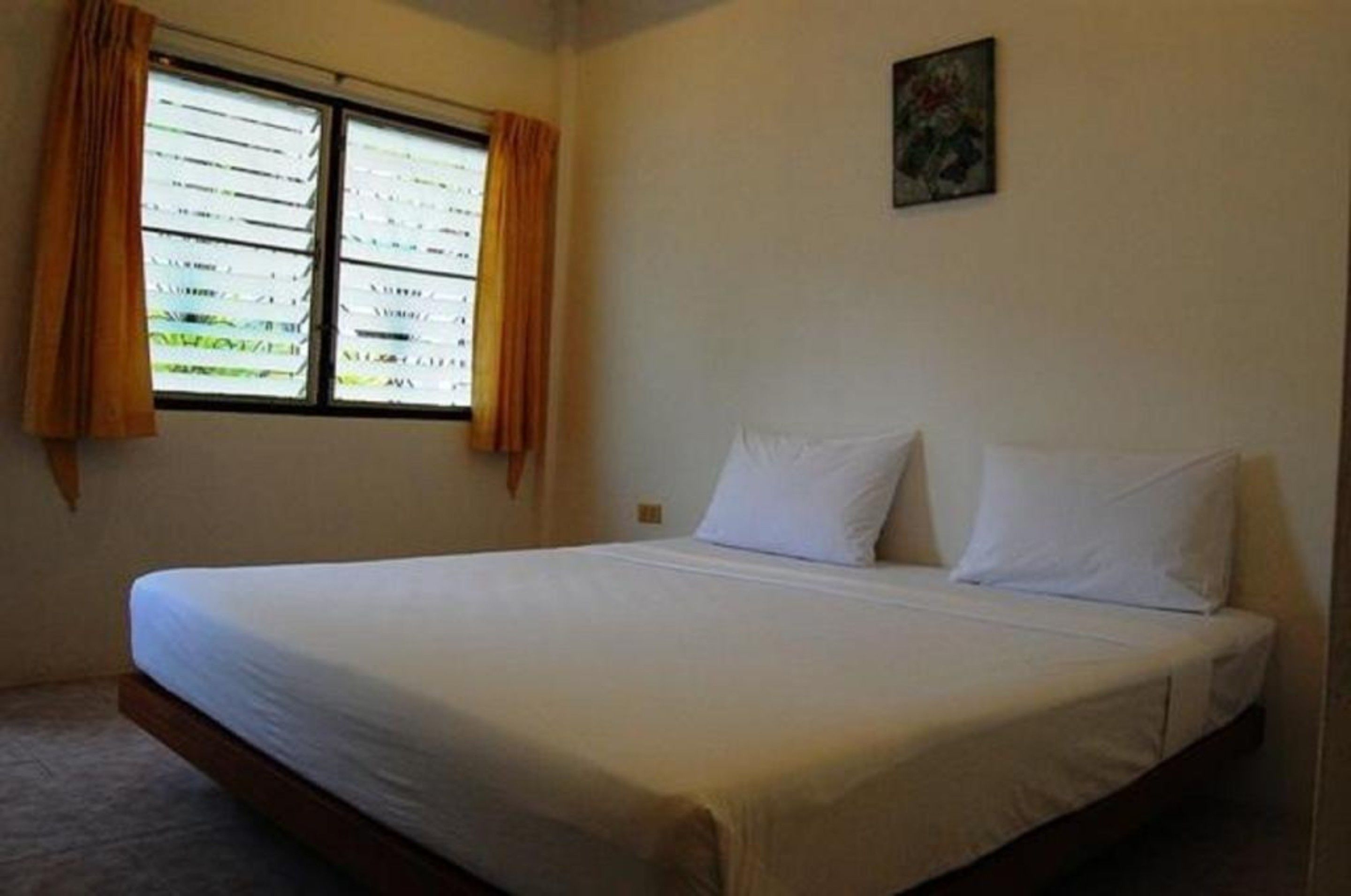 A simple room with a bed, a window with curtains, and a small painting on the wall.