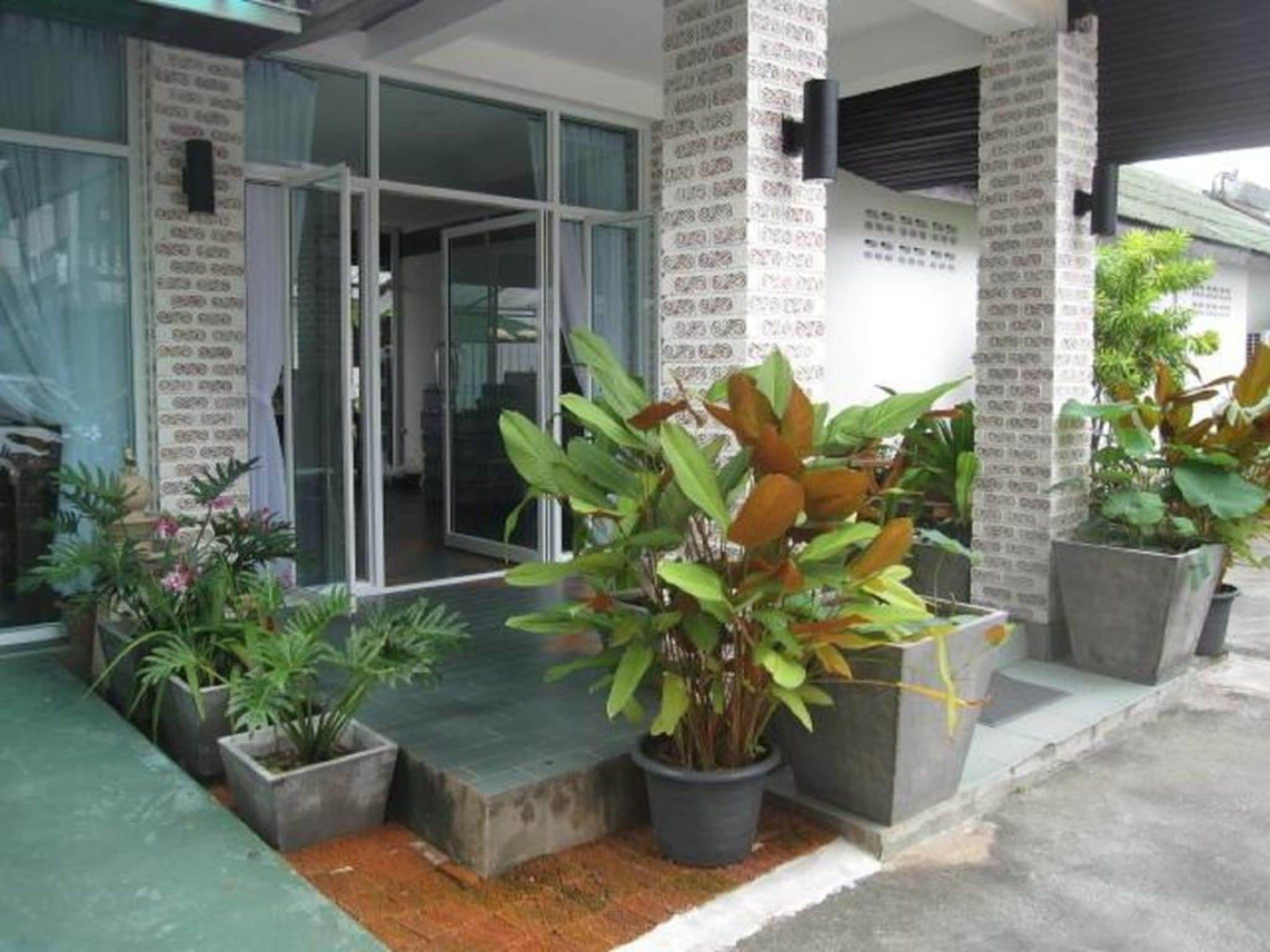 A modern building with large glass doors, potted plants, and a concrete pathway leading to the entrance.