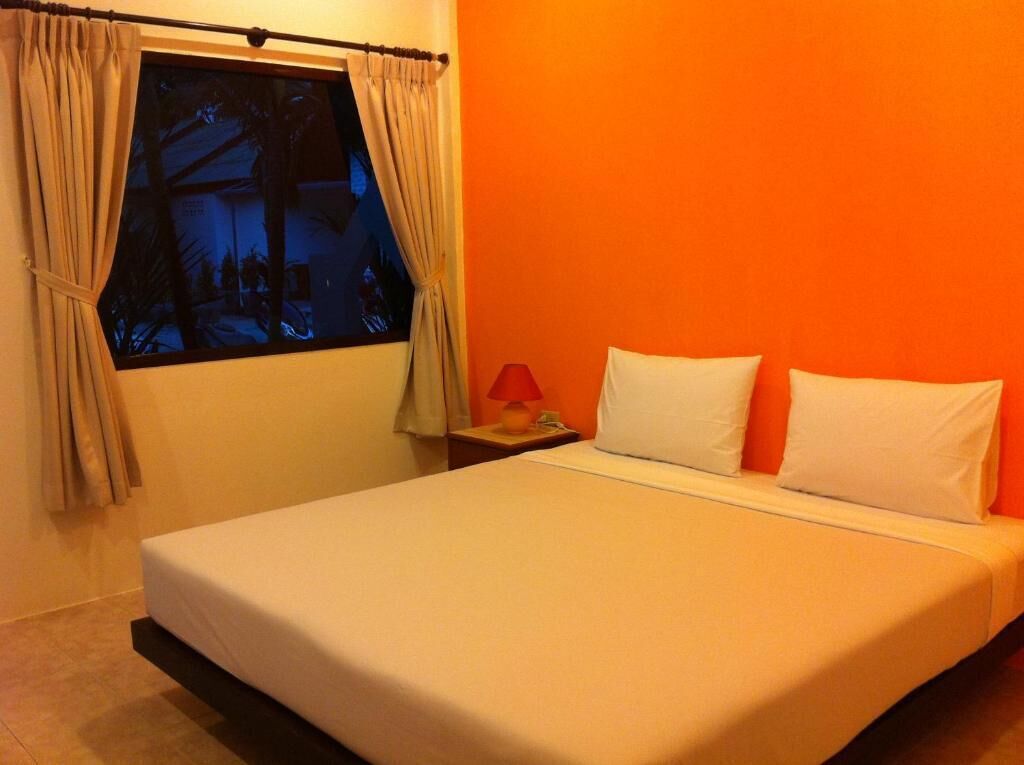 Una stanza con un letto, un comodino, una lampada e una finestra con tende.