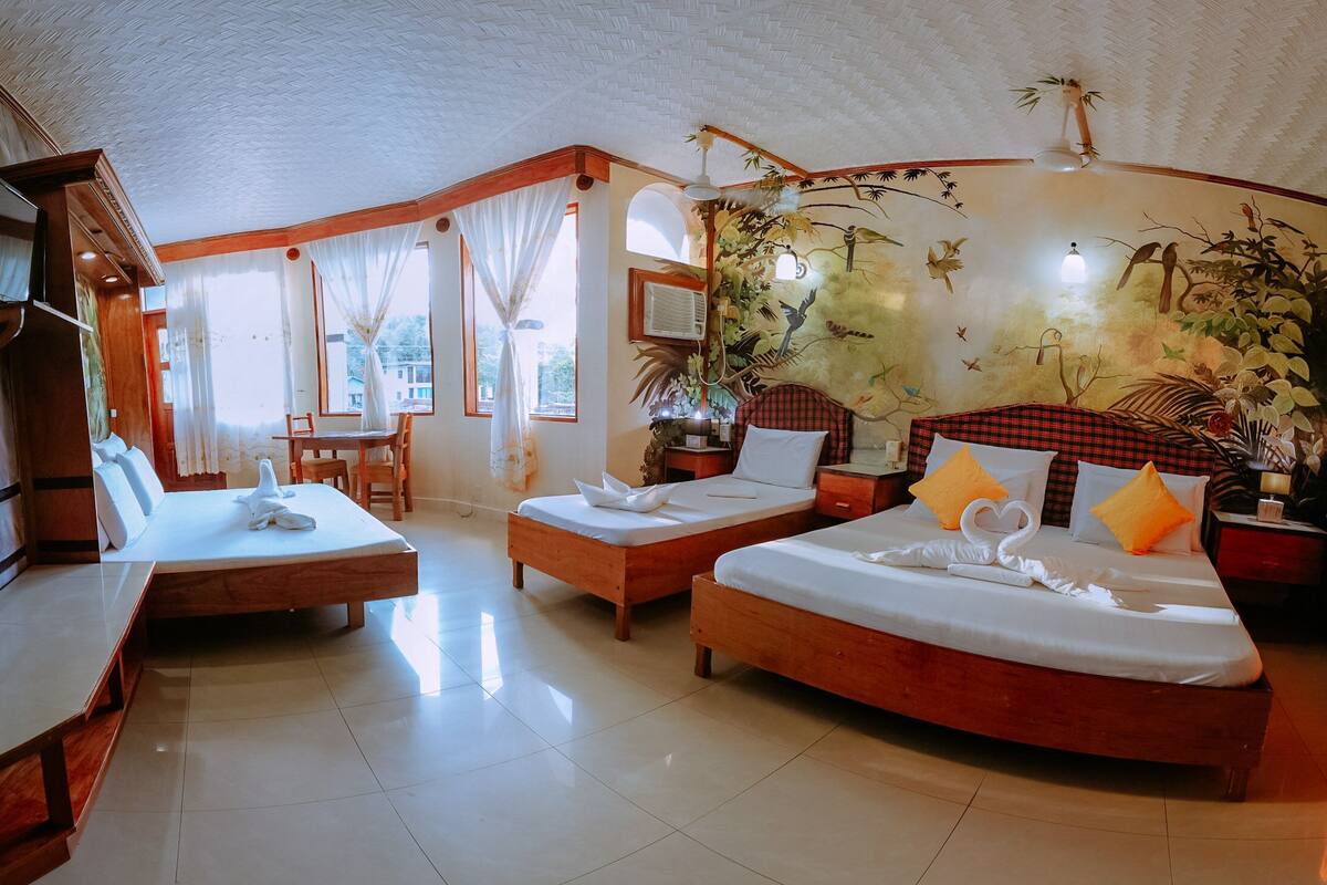 A hotel room with two beds, a dining area, and a large mural.