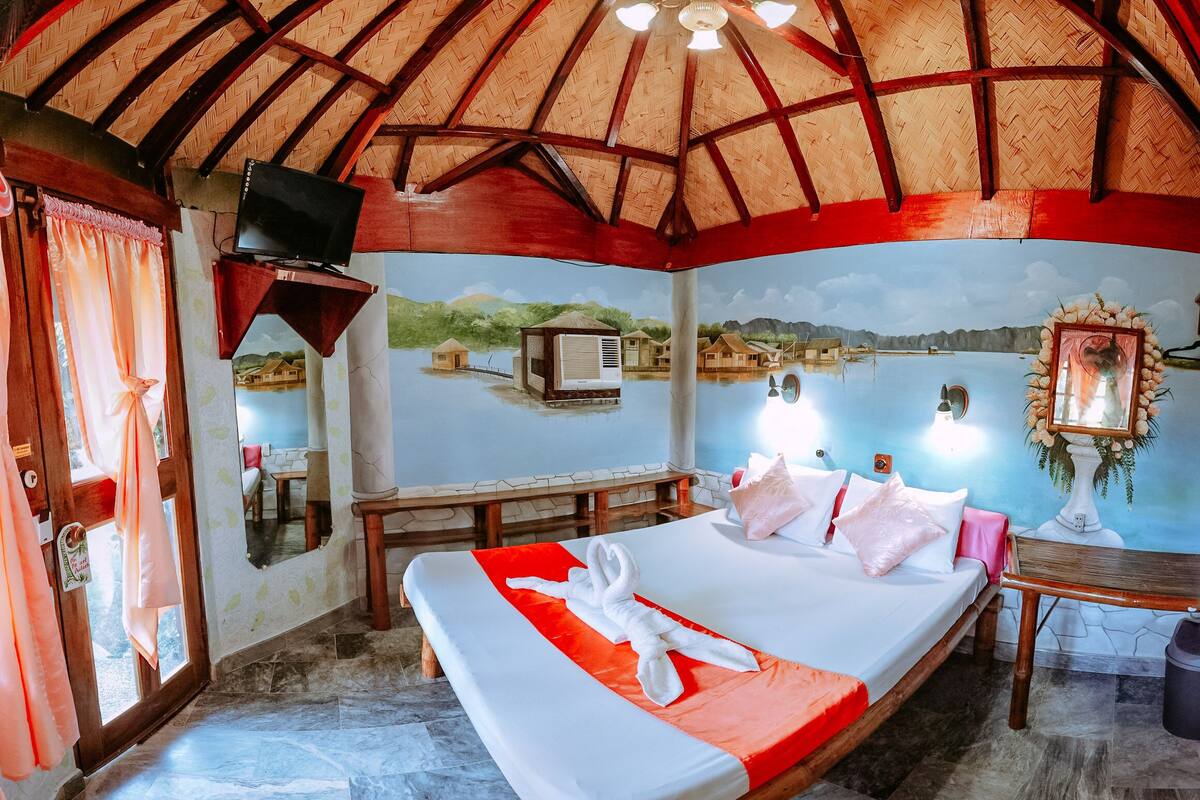 A room with a bed, a TV, a mural, and a view of water.