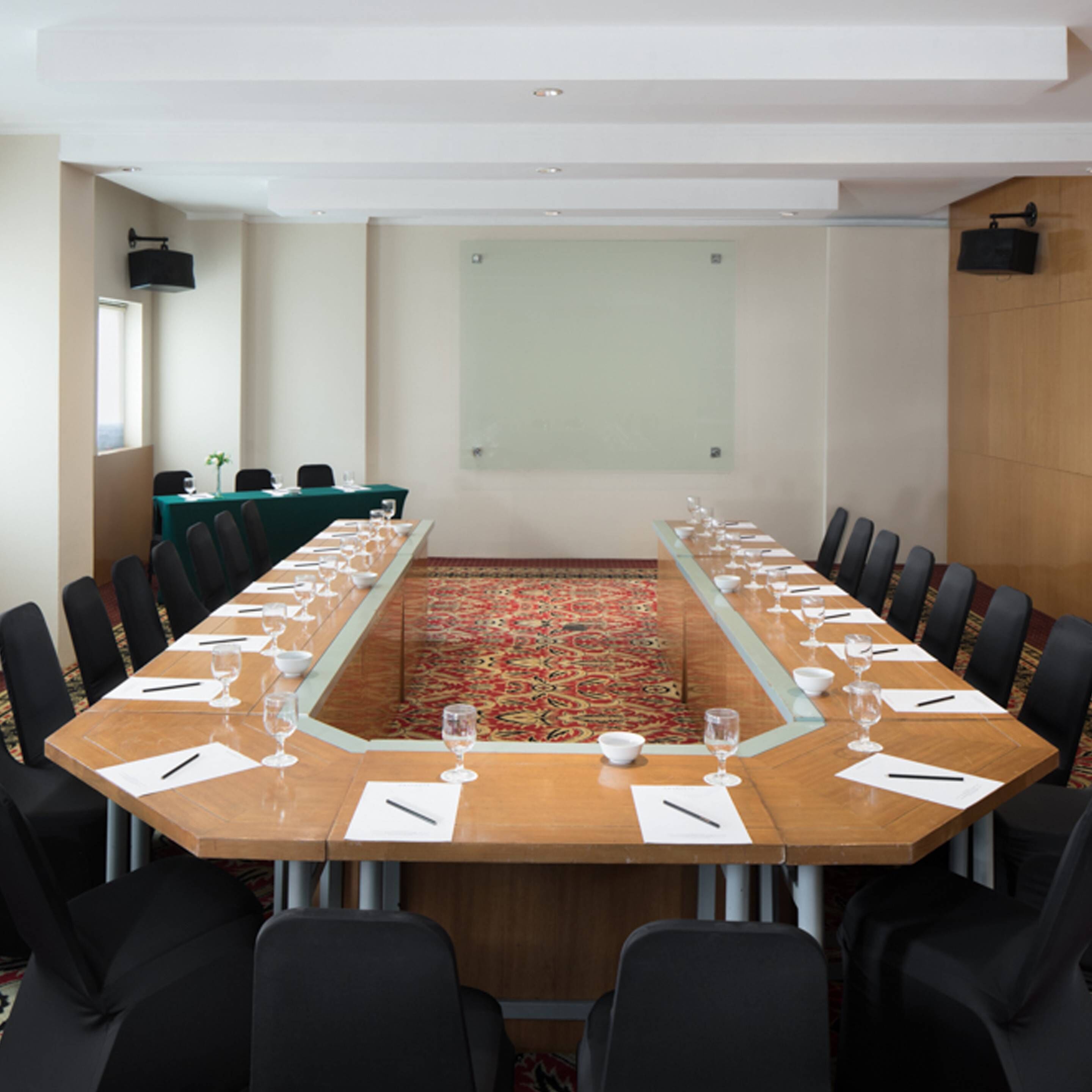 A conference room with a long table, black chairs, and a carpeted floor.