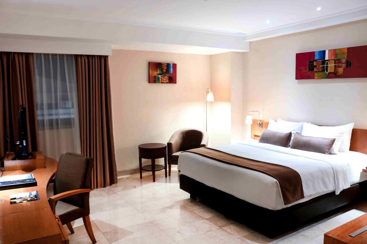 A hotel room with a large bed, a desk, a chair, and a small table.