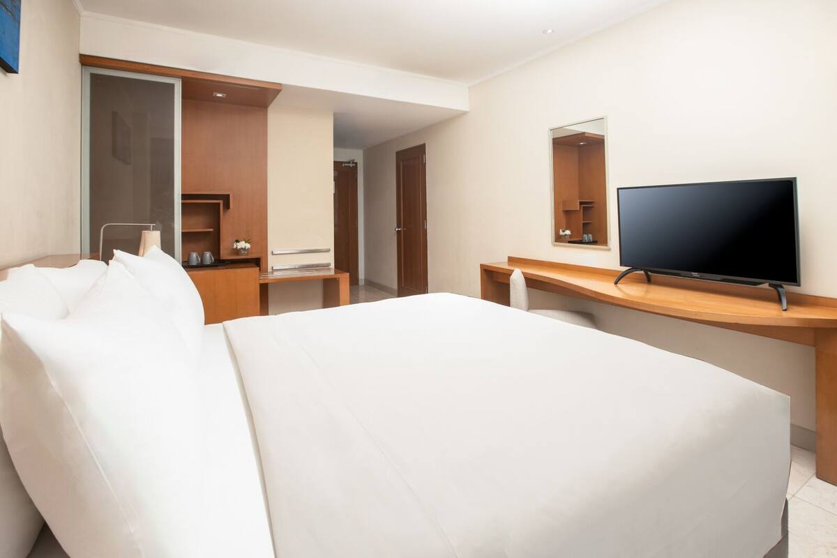 A hotel room with a bed, a desk, a television, and a mirror.