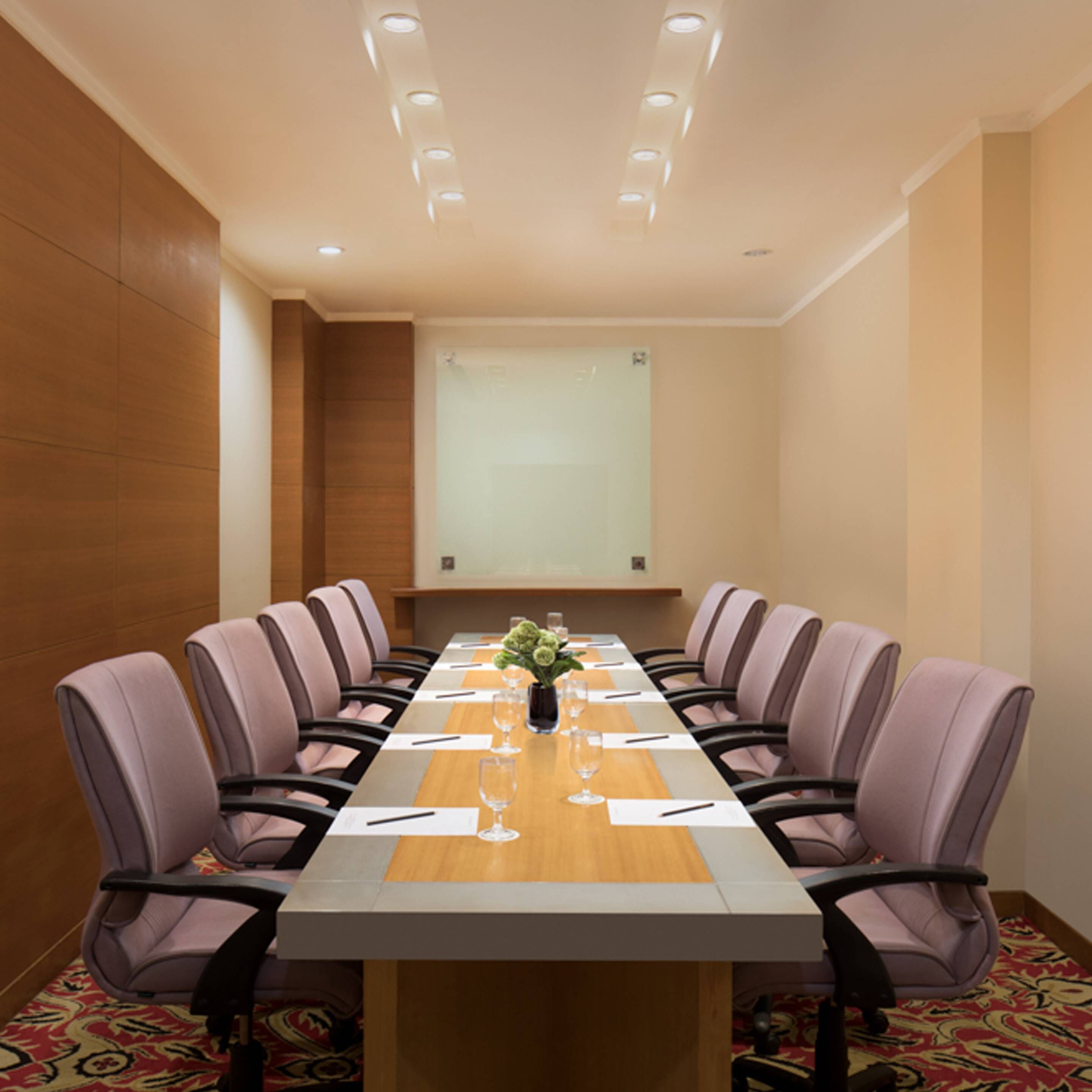 Un salón de conferencias con una larga mesa, seis sillas, una pantalla de proyector y un centro de mesa floral.