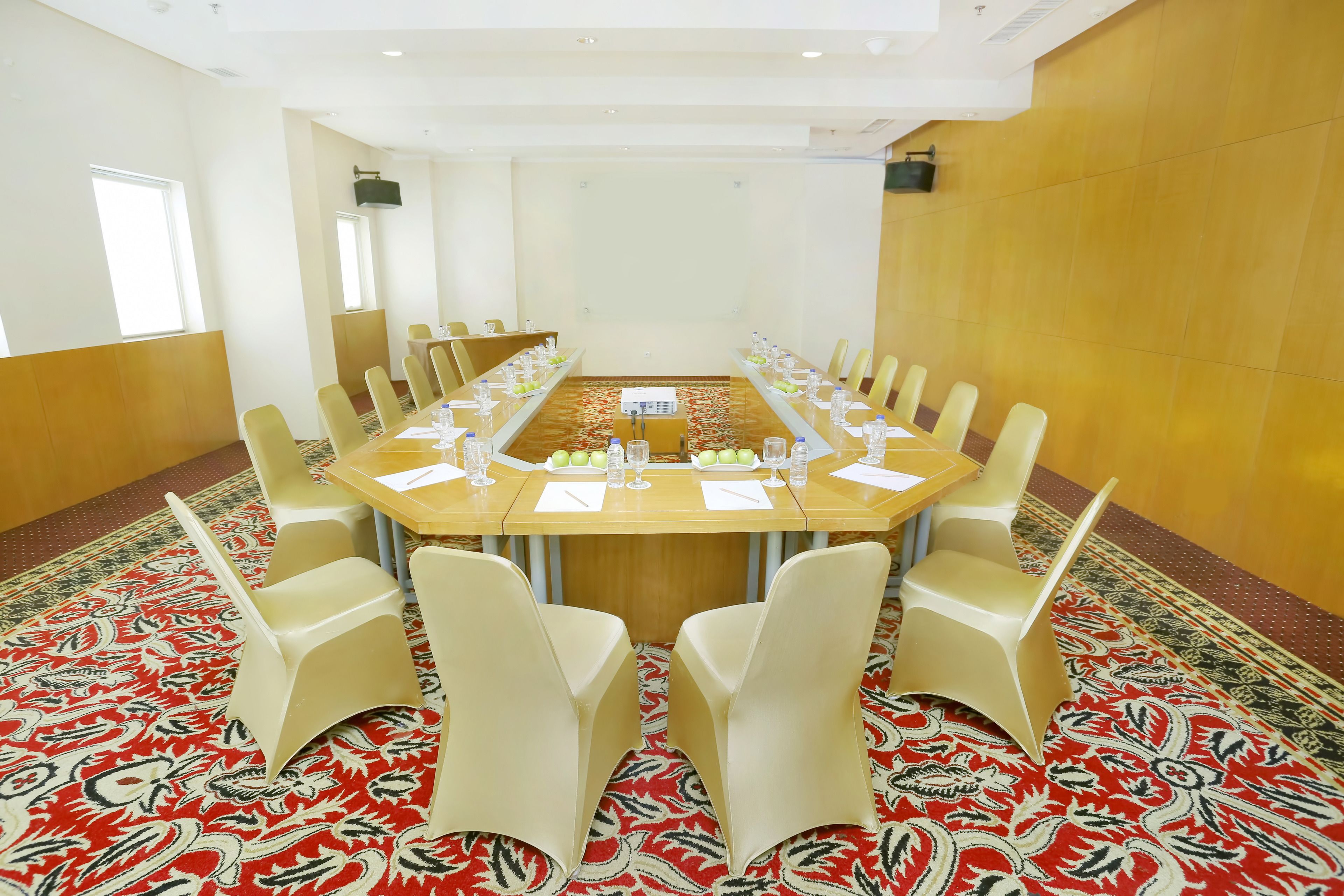 A conference room with a long table, beige chairs, and a patterned carpet.