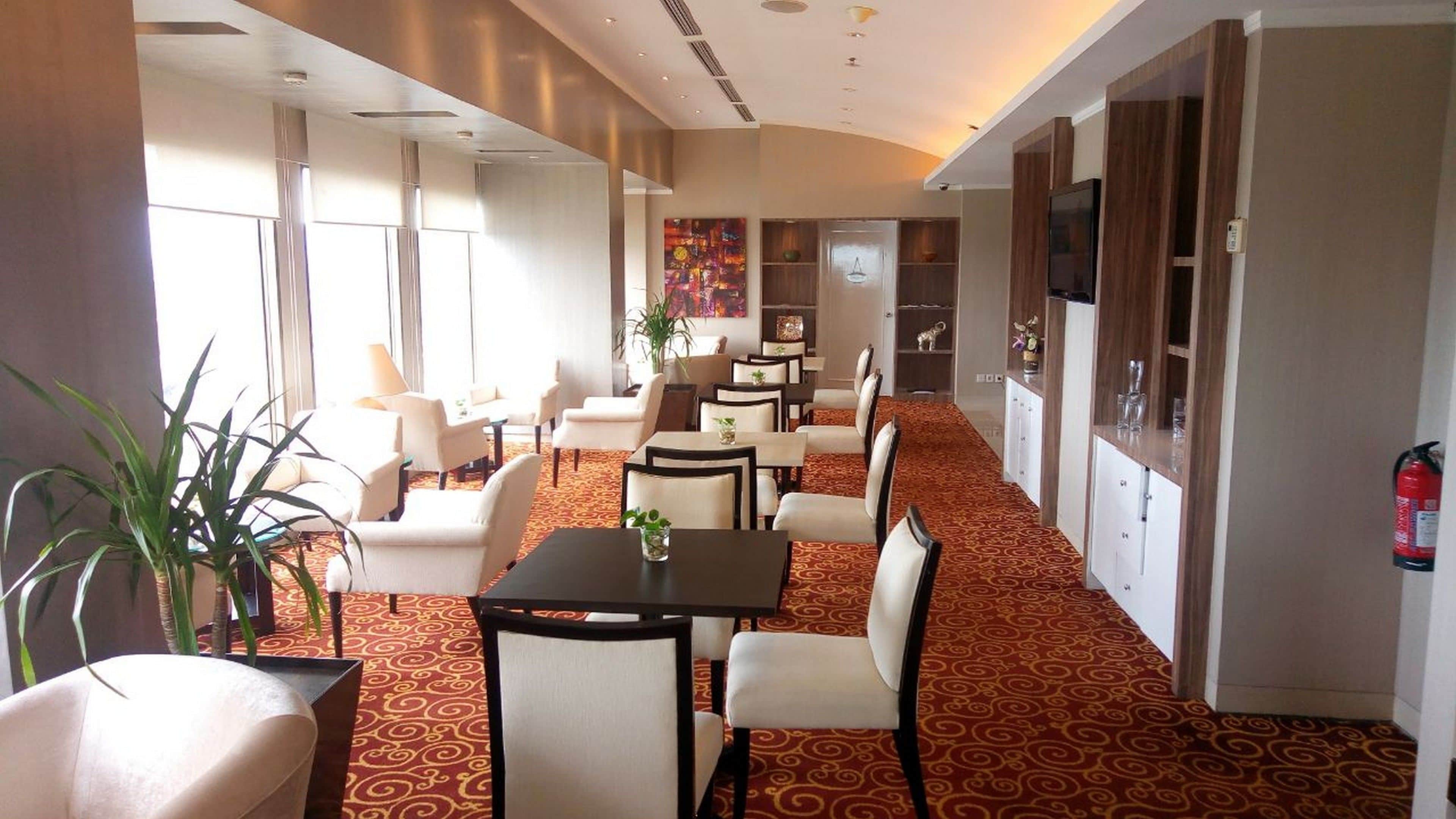 Um hall de hotel com uma longa mesa de jantar, várias cadeiras, um sofá e uma televisão na parede.