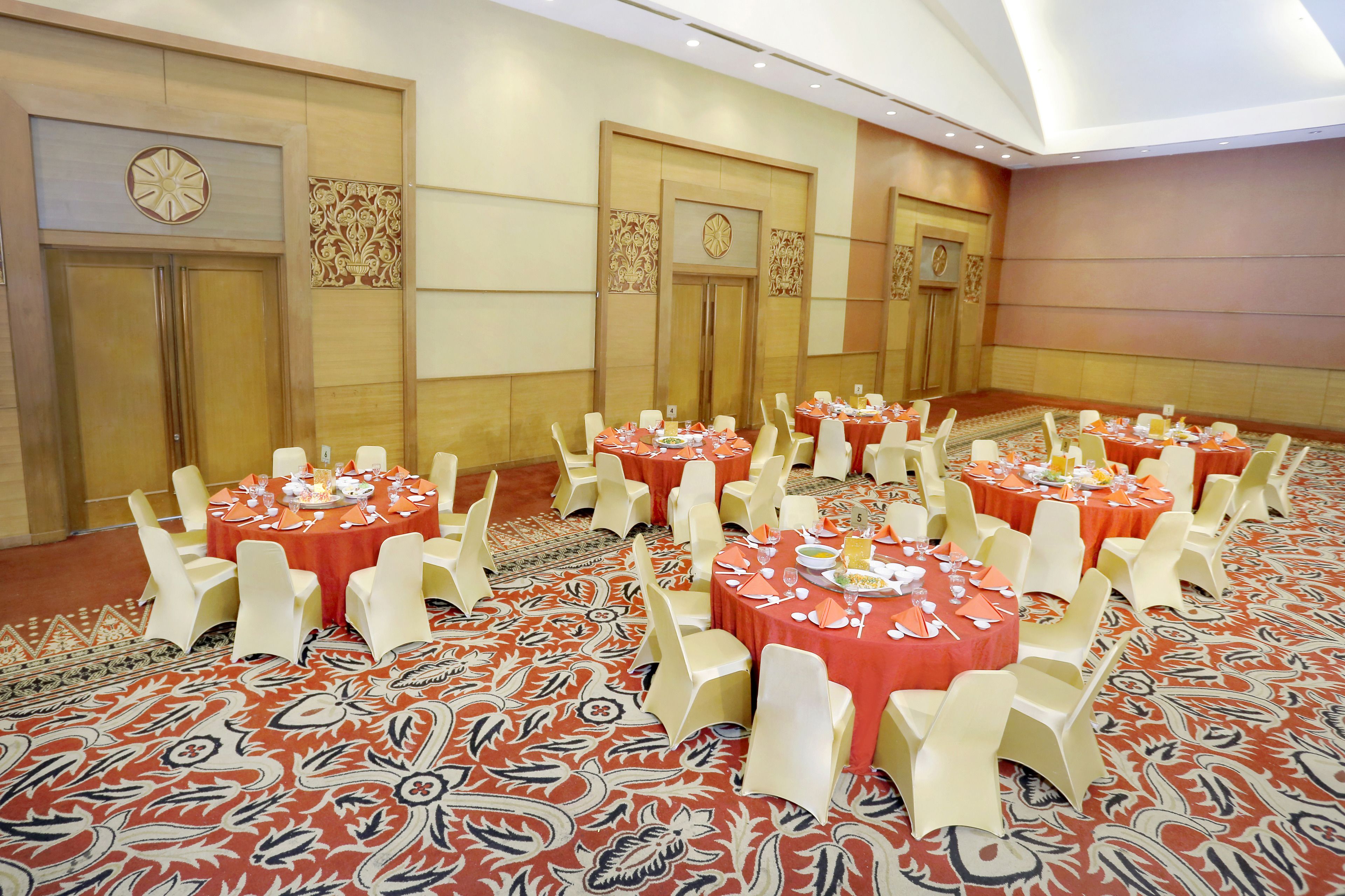 A banquet hall with round tables set for dining, white chairs, and a patterned carpet.