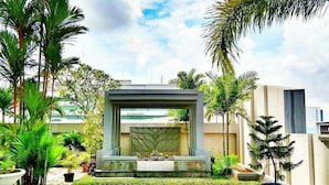 A modern outdoor area with a central water feature, surrounded by palm trees and potted plants.
