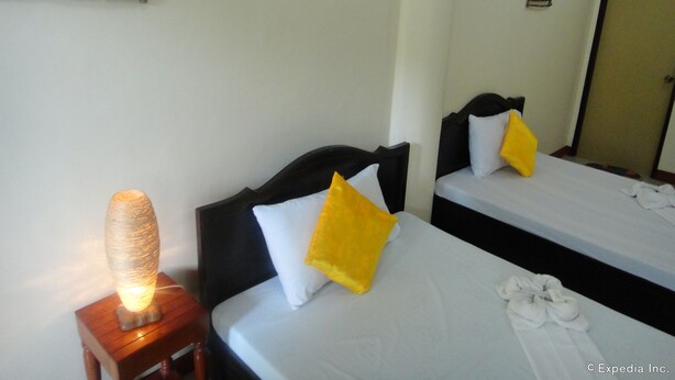 A hotel room with two beds, each with a white mattress and a black headboard. There is a bedside table with a lamp and a decorative item on it. - Amerson Pension Place - Hostel (Puerto Princesa)