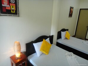 A hotel room with two beds, each with a white mattress and a black headboard. There is a bedside table with a lamp and a decorative item on it. - Amerson Pension Place - Hostel (Puerto Princesa)