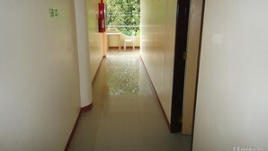A corridor with a window at the end, a chair, and a fire extinguisher on the wall. - Amerson Pension Place - Hostel (Puerto Princesa)