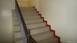 A staircase with a wooden handrail and red steps, leading to a landing with a yellow wall. - Amerson Pension Place - Hostel (Puerto Princesa)