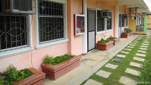 A building with multiple windows, some with metal bars, and potted plants along the walkway. - Amerson Pension Place - Hostel (Puerto Princesa)