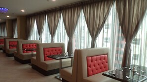 A row of seating areas with cushioned booths and tables, large windows with curtains, and a tiled floor. - Midcity Hotel Melaka (Malacca City)