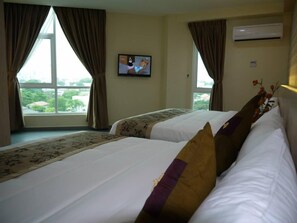 Ein Hotelzimmer mit zwei Betten, einem Fernseher an der Wand und Blick auf Grünfläche.