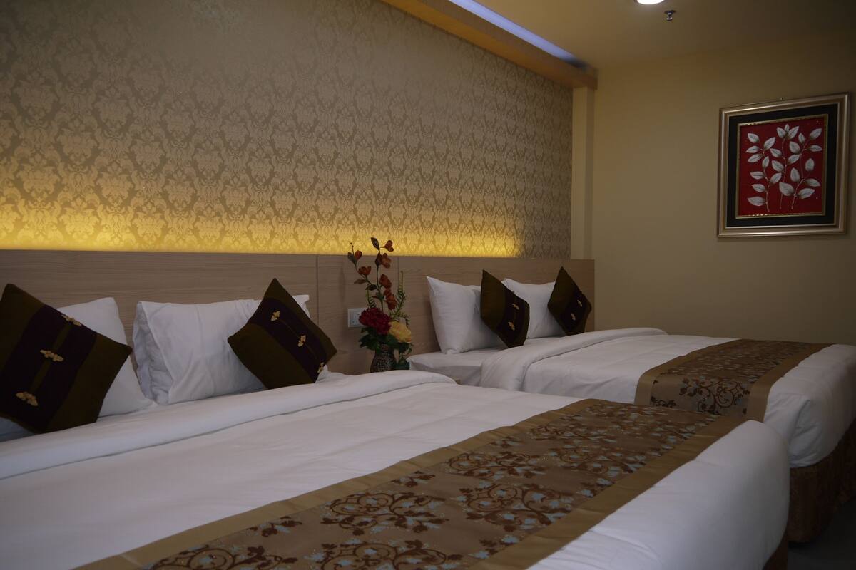 Habitación de hotel con dos camas, cada una con ropa de cama blanca y corredores decorativos marrones. En la mesita de noche entre las camas hay un jarrón con flores.