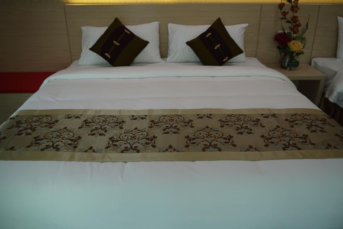 Habitación de hotel con una cama grande, dos almohadas, una mesita de noche con un jarrón de flores y una pared de acento roja.