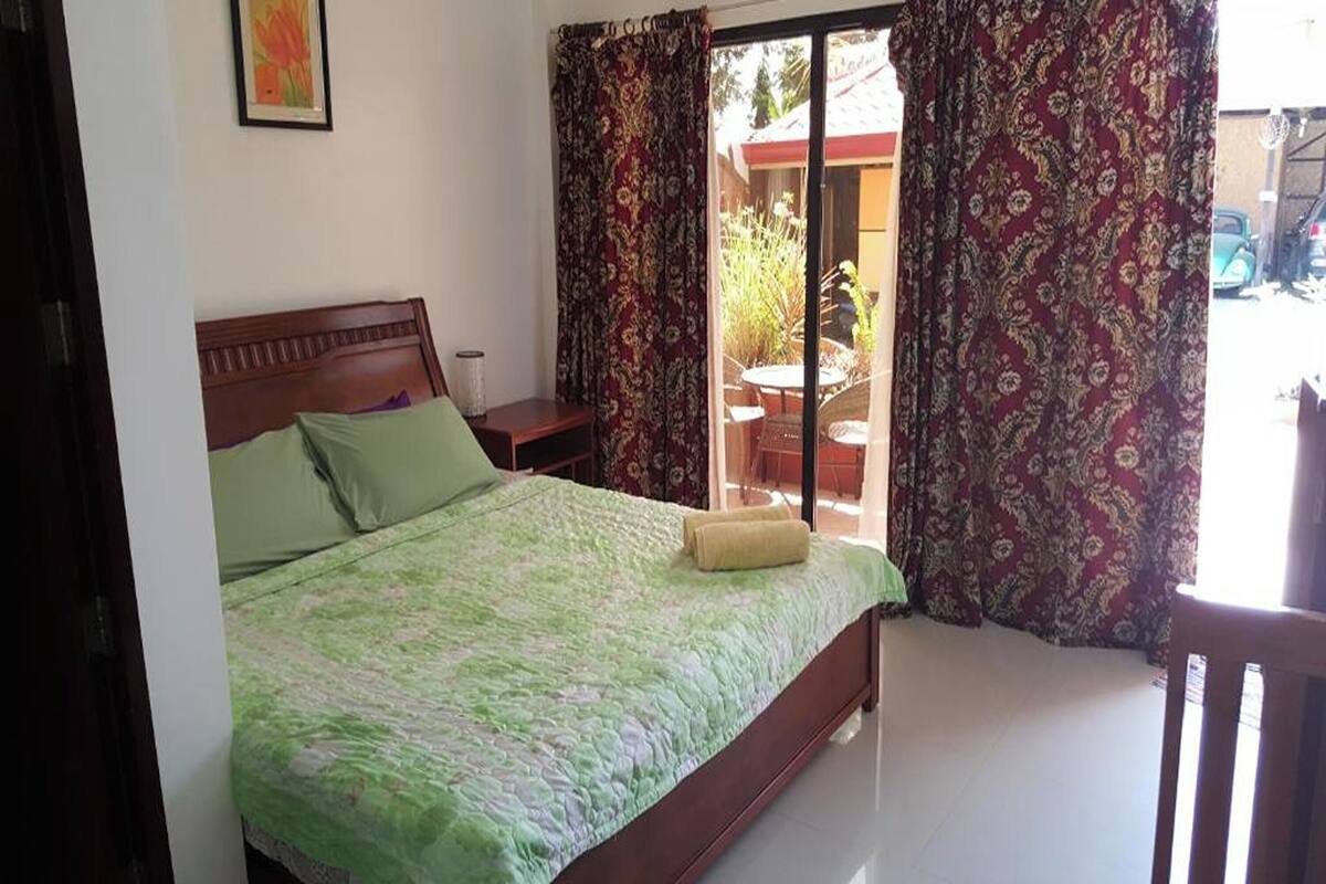A bedroom with a bed, a nightstand, a window with curtains, and a view of the outside.