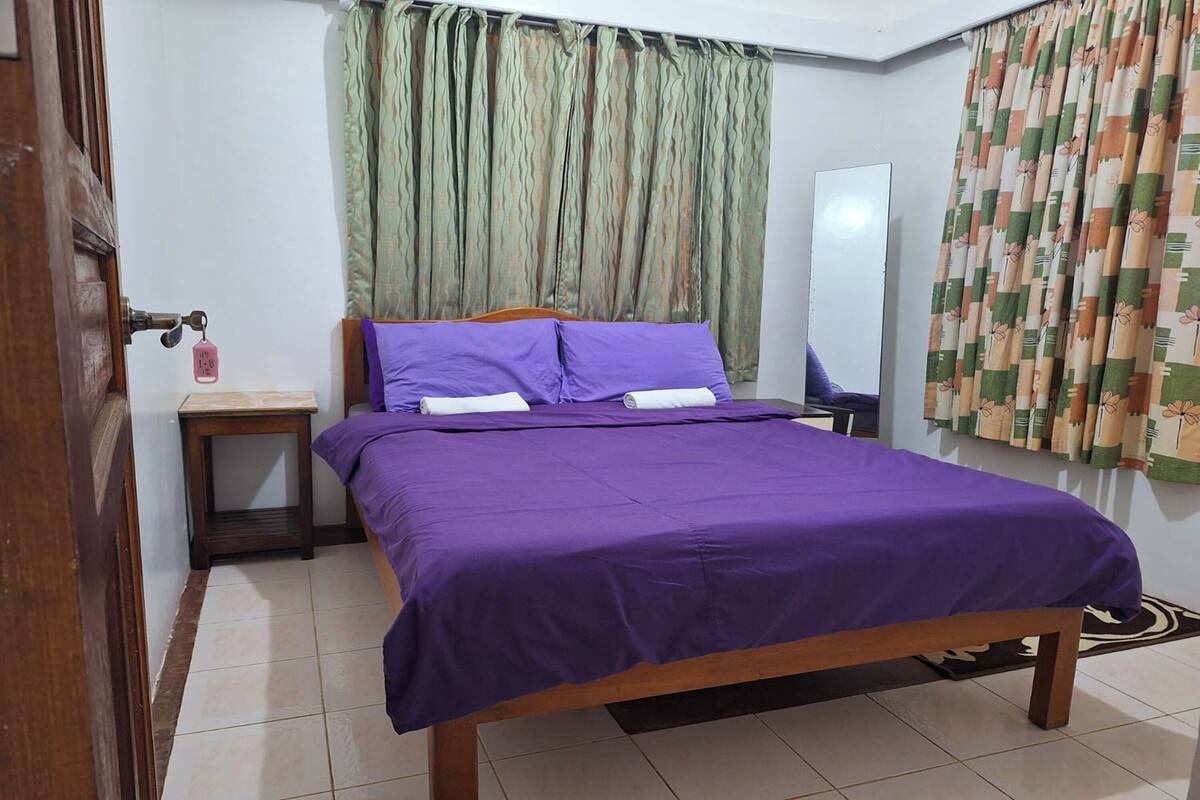 A bedroom with a bed, a nightstand, a mirror, and curtains.