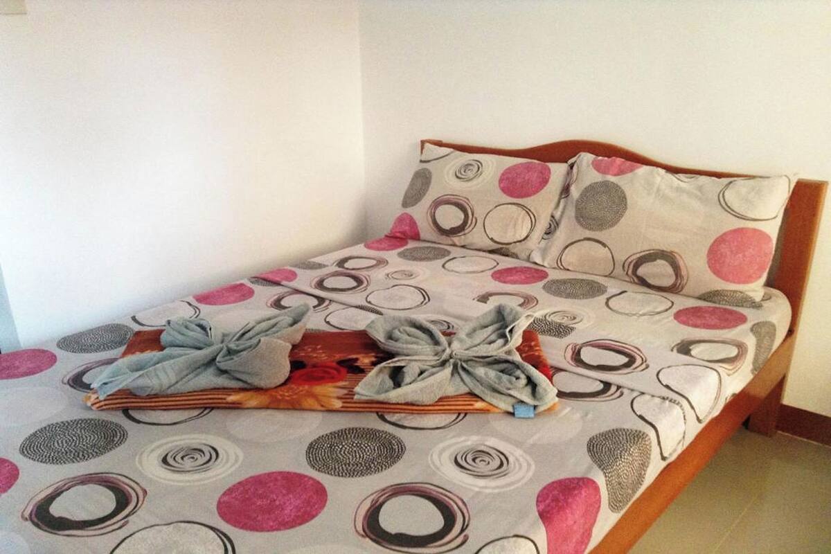 A neatly made bed with a polka dot bedspread and pillows, a wooden headboard, and a folded towel on the bed.