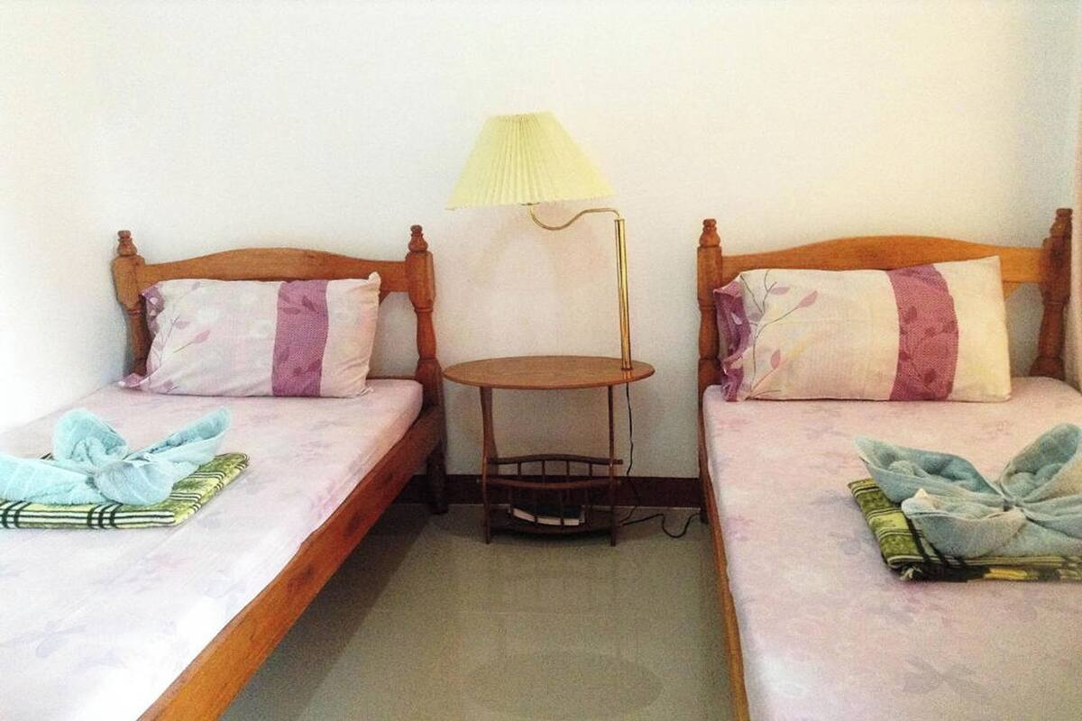 A room with two single beds, each with a wooden headboard, a small round table, and a lamp between them.