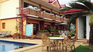 A pool area with a signboard, outdoor seating, and a staircase leading to a balcony. - Citadel Bed and Breakfast (Puerto Princesa)