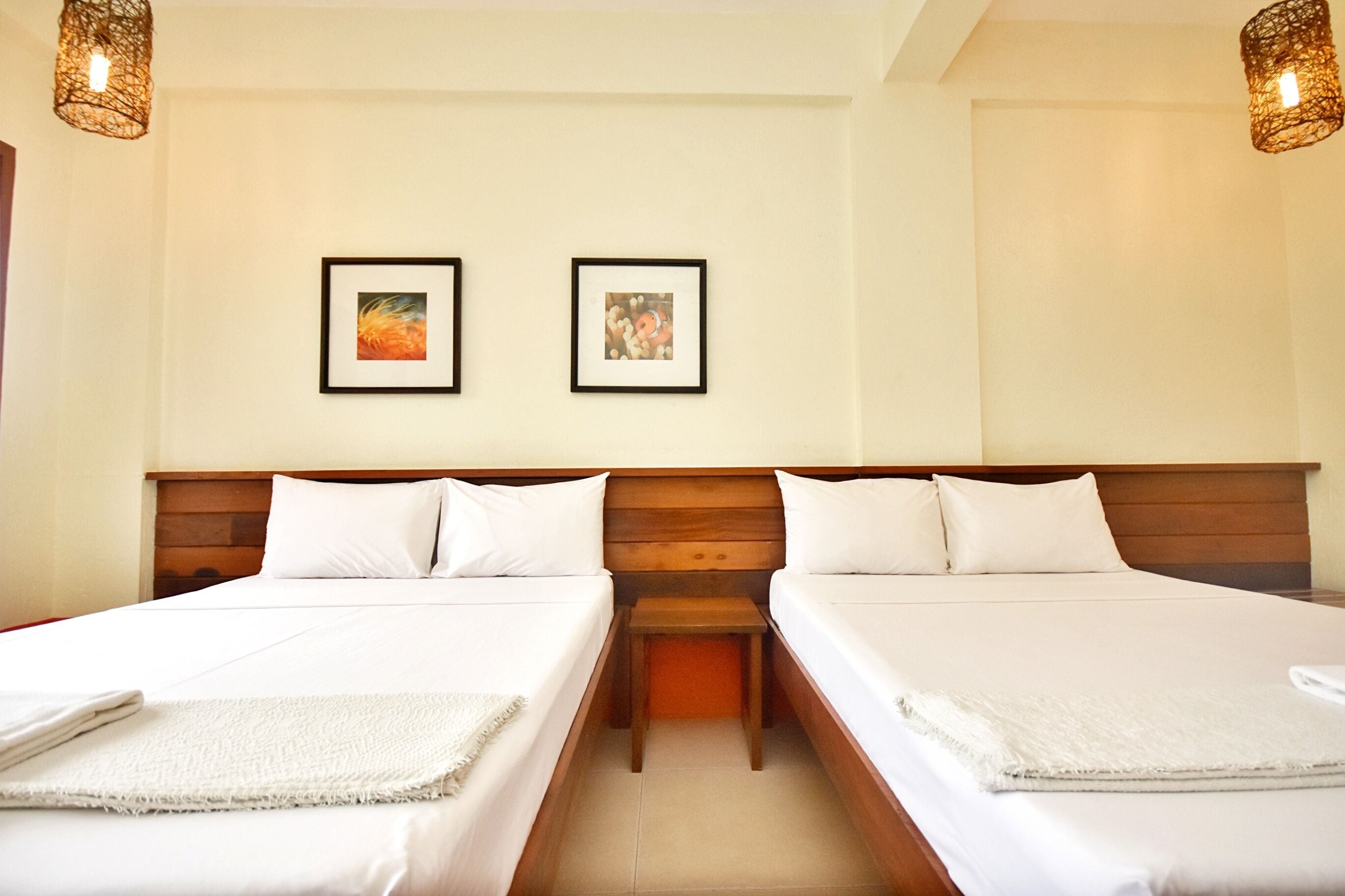 A hotel room with two beds, a wooden headboard, a small bedside table, and two framed pictures on the wall.