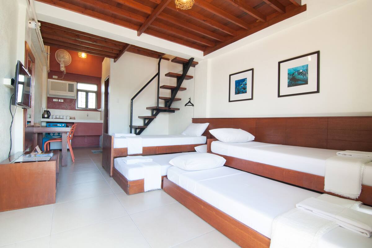 Una habitación de hotel moderna con escalera de madera, kitchenette y una cama grande con ropa de cama blanca.
