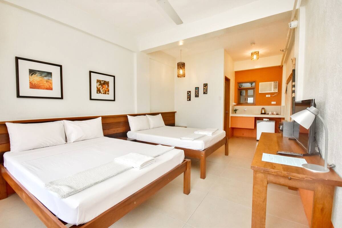 Habitación de hotel con dos camas, un escritorio de madera, un televisor y un baño visible a través de una puerta abierta.