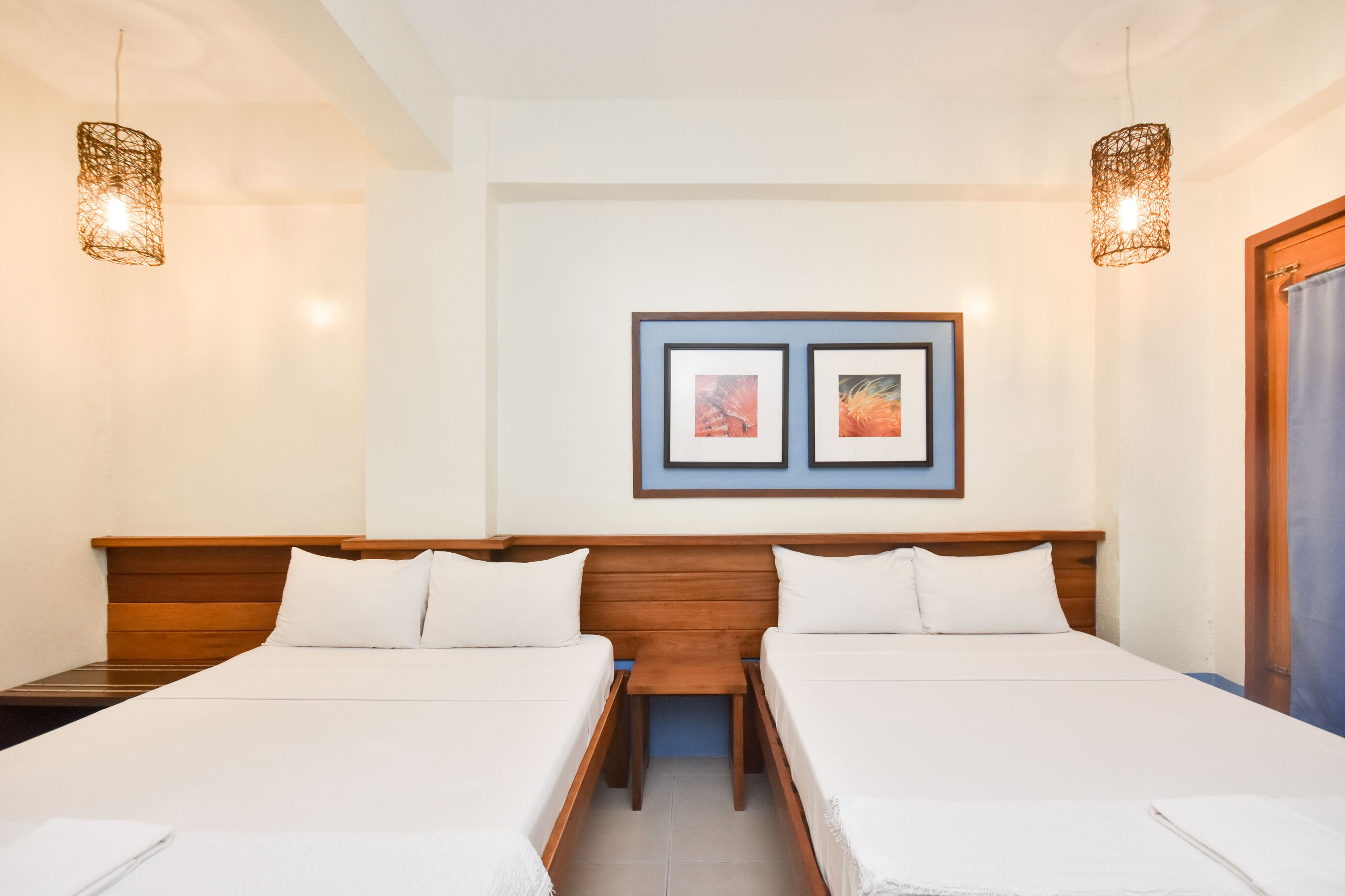 Habitación de hotel con dos camas, un cabecero de madera, una mesita y dos cuadros enmarcados en la pared.