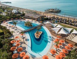 A resort with a large swimming pool, beach umbrellas, and a pier.