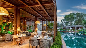 Un espace extérieur aménagé pour les repas, avec des tables et des chaises, une piscine et une végétation luxuriante.