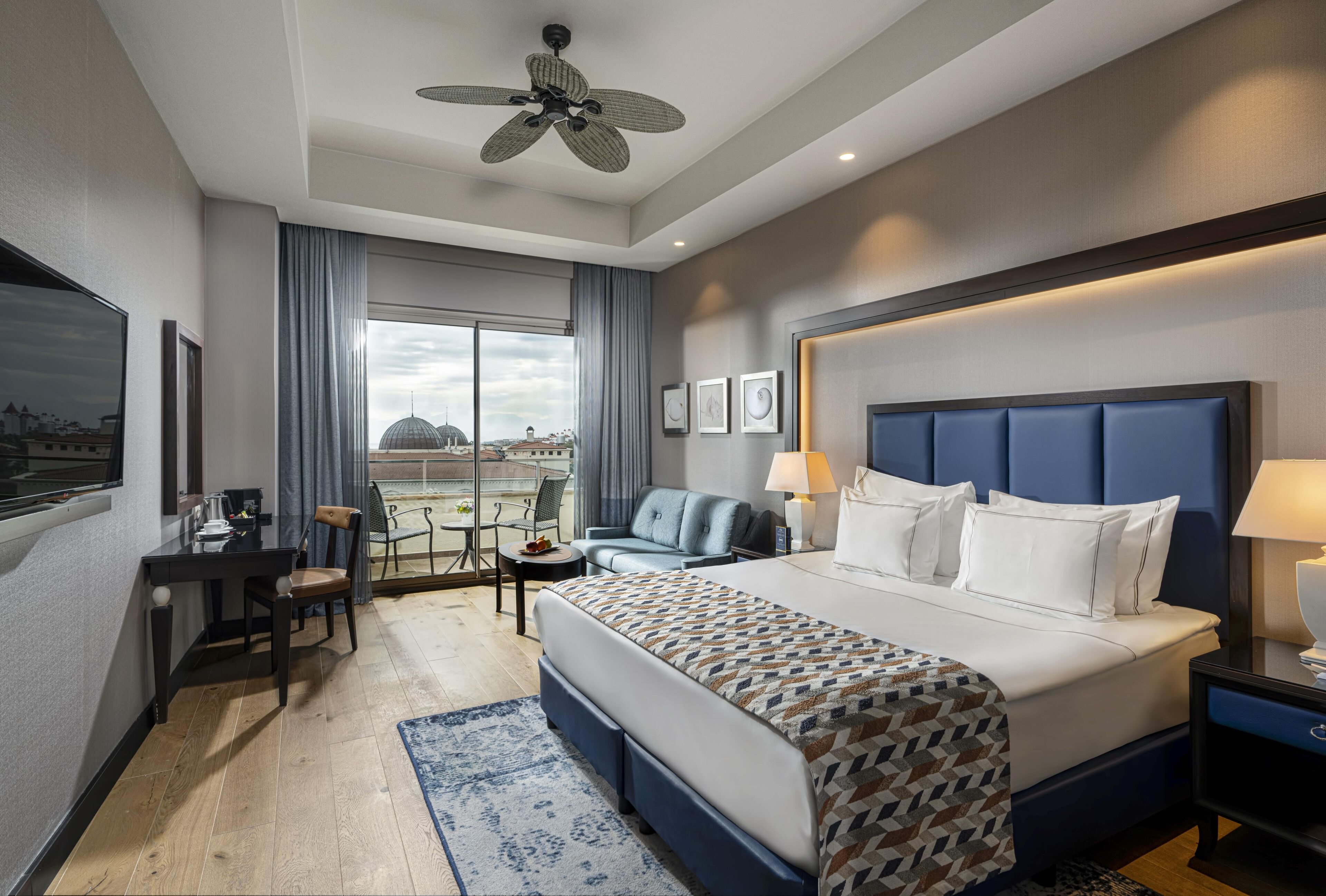 A hotel room with a bed, desk, chair, and a view of the cityscape.