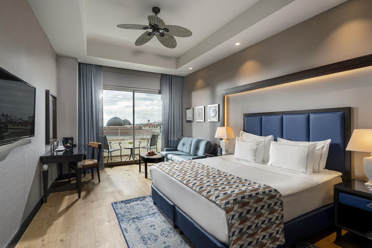 A hotel room with a bed, desk, chair, and a view of the cityscape.