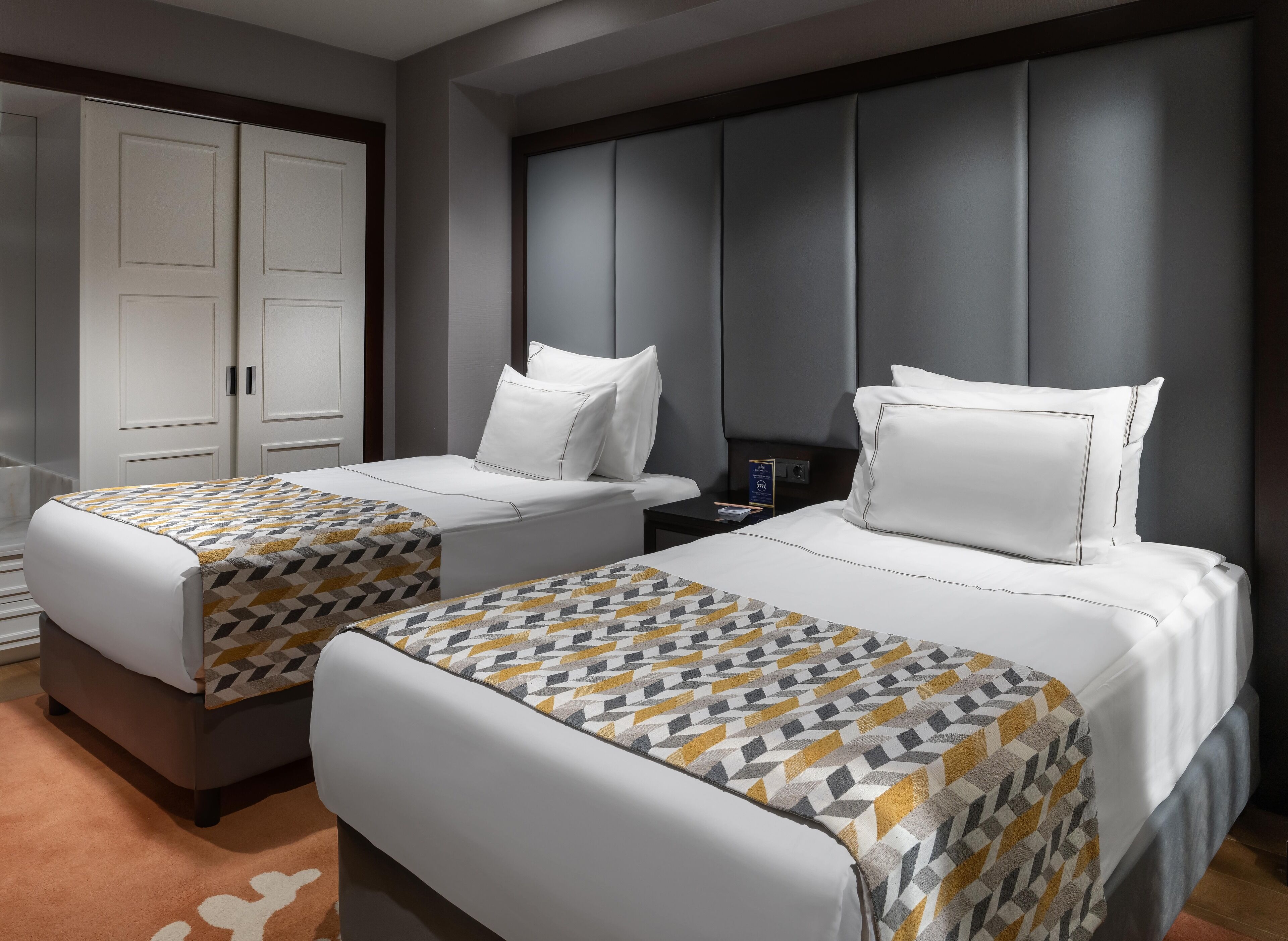 A hotel room with two beds, a wardrobe, and a nightstand with a lamp.
