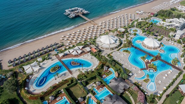 Vue aérienne d’un complexe hôtelier doté de plusieurs piscines, de parasols installés sur la plage et d’une jetée qui s’avance dans l’océan.